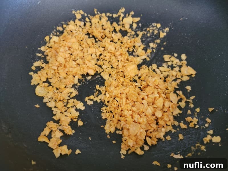 Crushed corn flake pieces and melted butter being stirred together in a skillet for the cheesy green beans topping.
