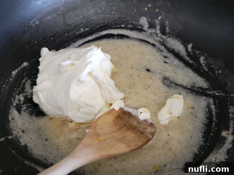 Sour cream melting into the butter and flour mixture in a black skillet, creating a creamy base for cheesy green beans.