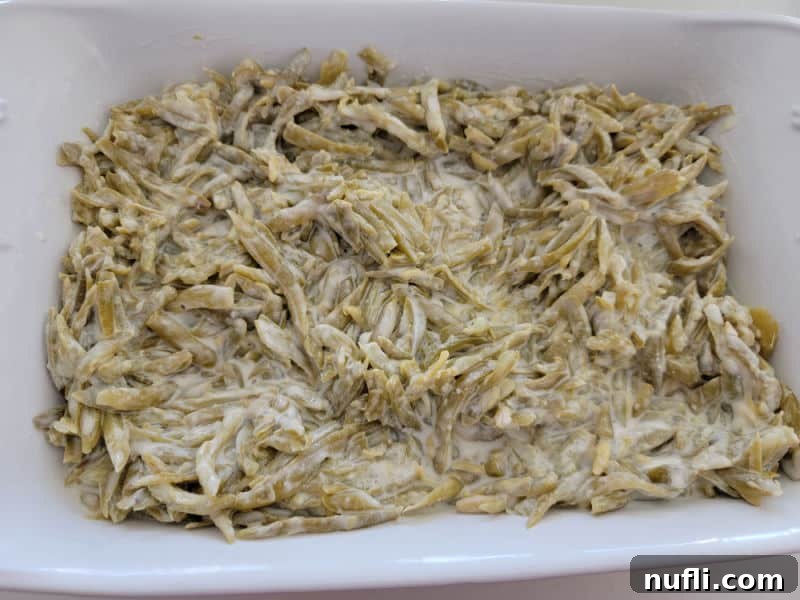 Sour cream coated green beans poured into a white casserole dish, ready for topping.