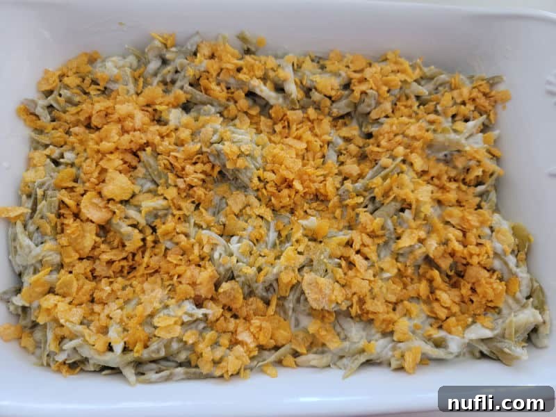 Buttery cornflake mixture evenly sprinkled over the green beans in a white casserole dish.