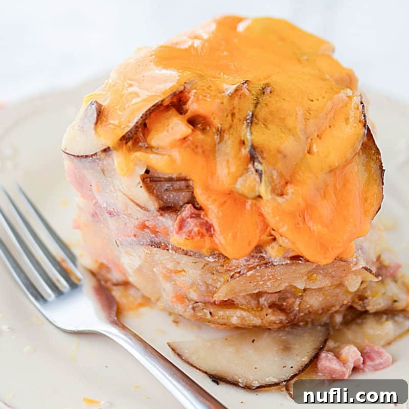 cheese melting over scalloped potatoes and ham on a white plate with a silver fork.
