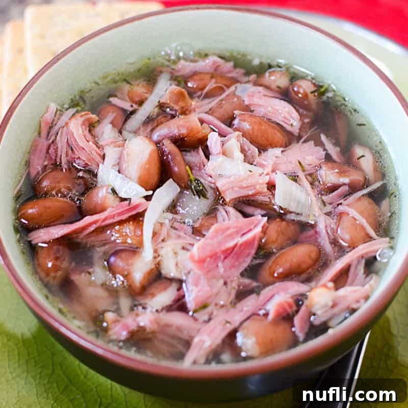 Ham and bean soup in a white bowl next to crackers on a green plate