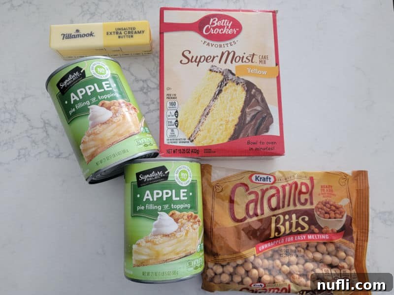 The four simple ingredients laid out for Caramel Apple Dump Cake: two cans of apple pie filling, sticks of butter, a box of yellow cake mix, and a bag of caramel bits.