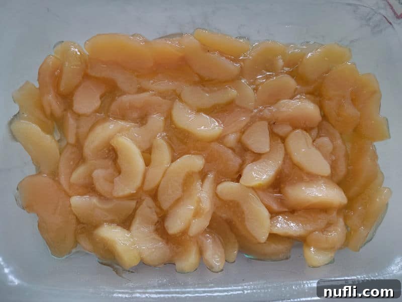 Apple pie filling spread evenly across the bottom of a greased glass casserole dish, forming the foundational layer for the caramel apple dump cake.