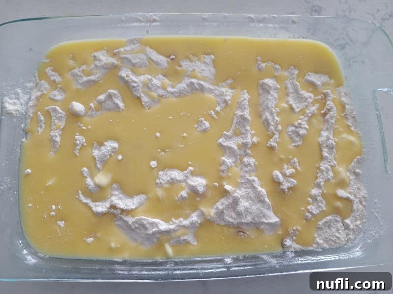 Melted butter being slowly and evenly poured over the dry cake mix layer in a glass baking dish, preparing the caramel apple dump cake for baking.