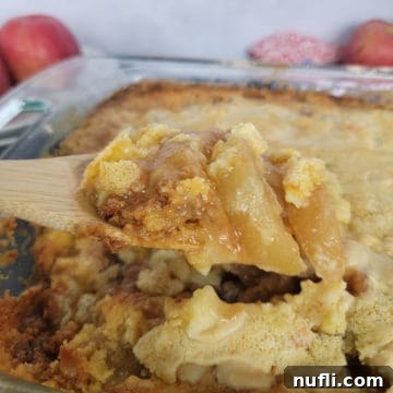 Wooden spoon scooping Caramel Apple Dump Cake from a glass pan, showing the rich, gooey layers of apple and caramel with a golden cake topping.