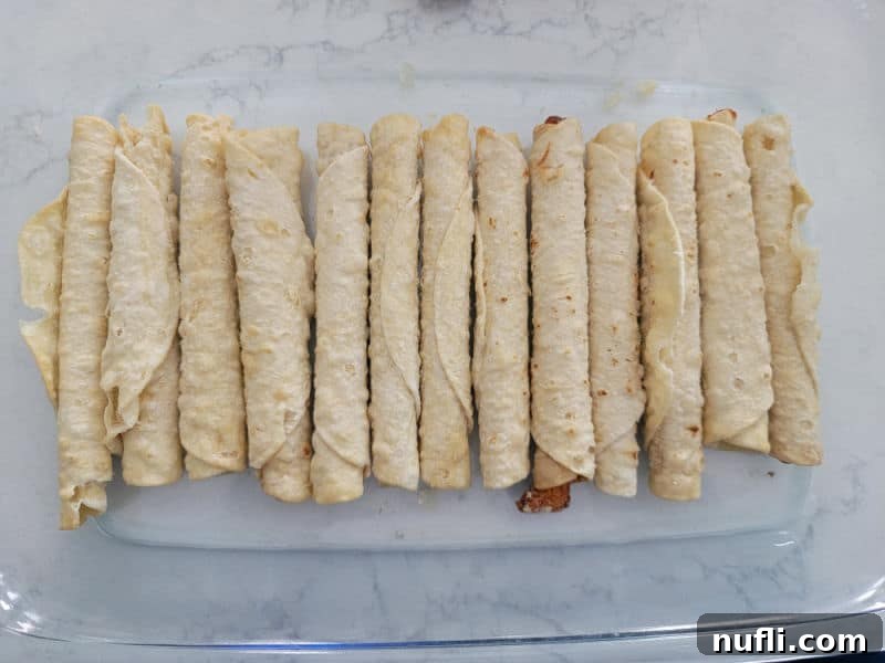 Frozen taquitos spread in a glass baking dish for Taquito enchiladas