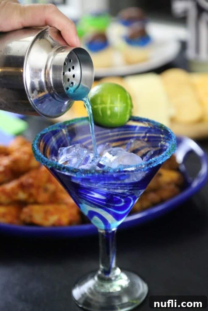 Blue cocktail pouring into a martini glass with a football lime