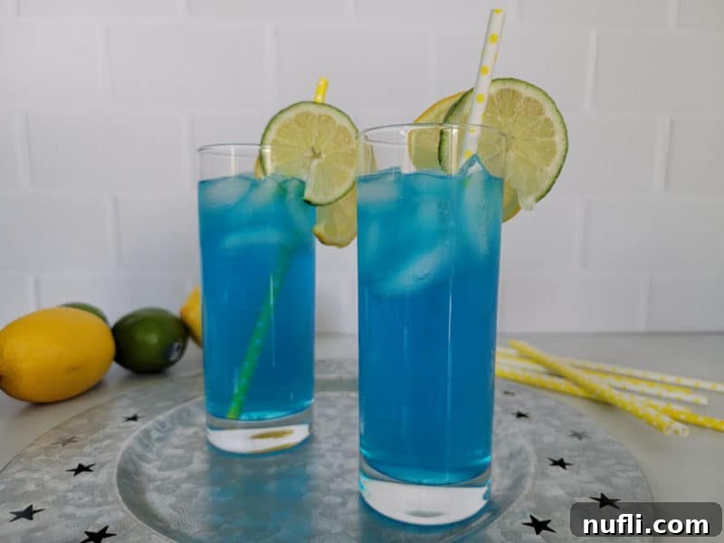 Two electric blue lemonade cocktails on a silver platter with yellow straws and lemon and limes