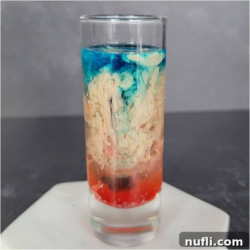 Blue Cream and Red alien brain hemorrhage shot in a clear glass on a white coaster.