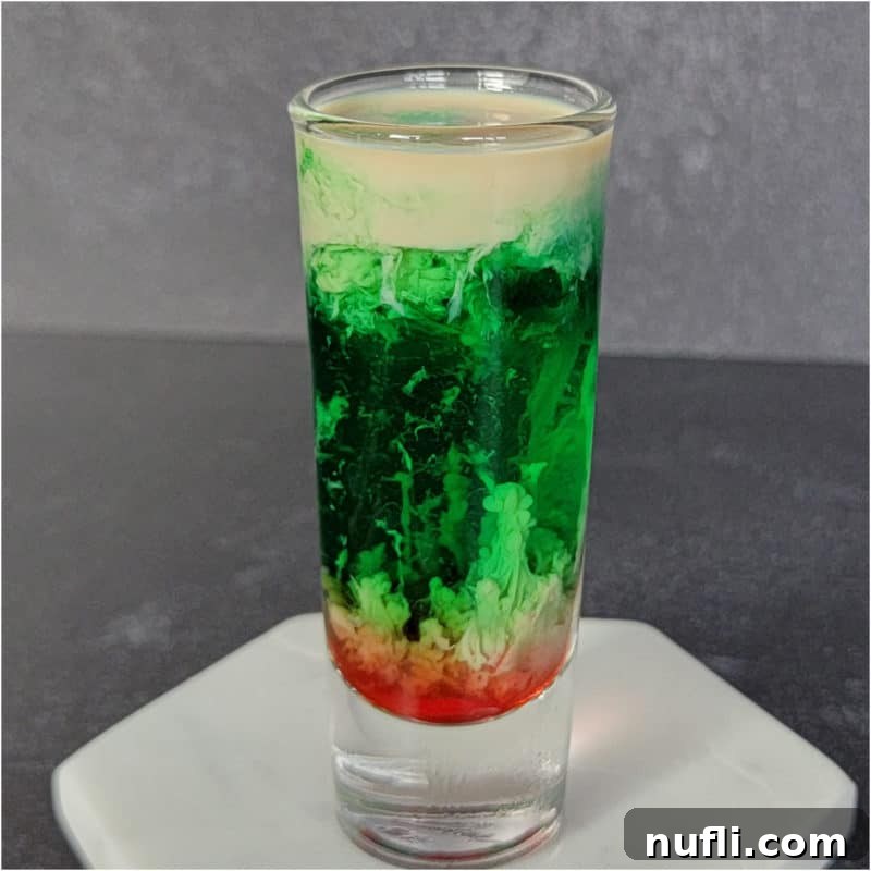 The Ultimate Guide to Peach Schnapps Cocktails 14 Cream Green and red Zombie Brain Shot in a clear shot glass on a white coaster.