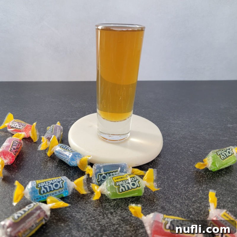 The Ultimate Guide to Peach Schnapps Cocktails 10 Jolly Ranch Shot on a white coaster surrounded by Jolly Rancher Candy