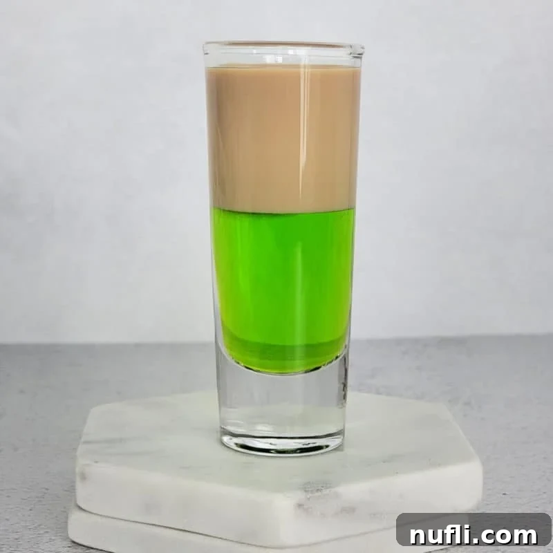 Midori Mixology: Your Ultimate Guide 6 A visually striking layered brown and green cocktail shot, elegantly presented on two white coasters.