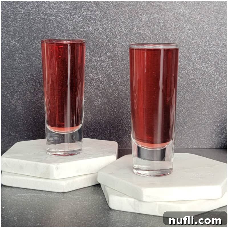 Two red cocktail shots on white coasters.