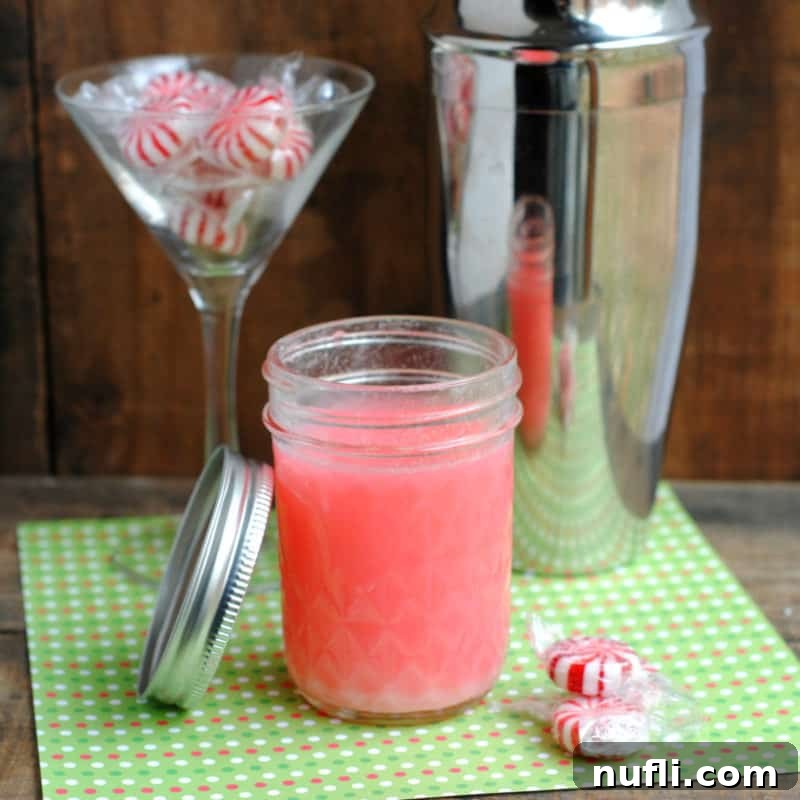 Peppermint vodka in a mason jar next to a martini glass with peppermint candies and a silver cocktail shaker
