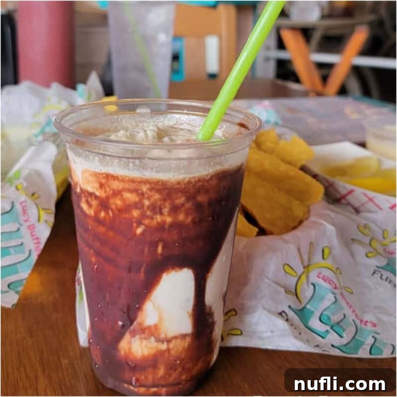 Chocolate Bushwacker served in a plastic cup with a green straw, with Lulu's chips and salsa nearby