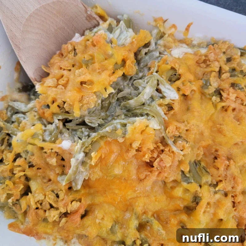 A wooden spoon scooping up Cheesy Green Beans from a white casserole dish.