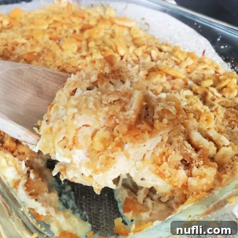 A golden Ritz Cracker topped chicken casserole in a glass dish with a wooden spoon for serving.