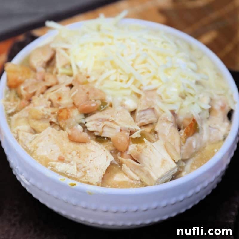A steaming bowl of White Chicken Chili, garnished with shredded cheese.