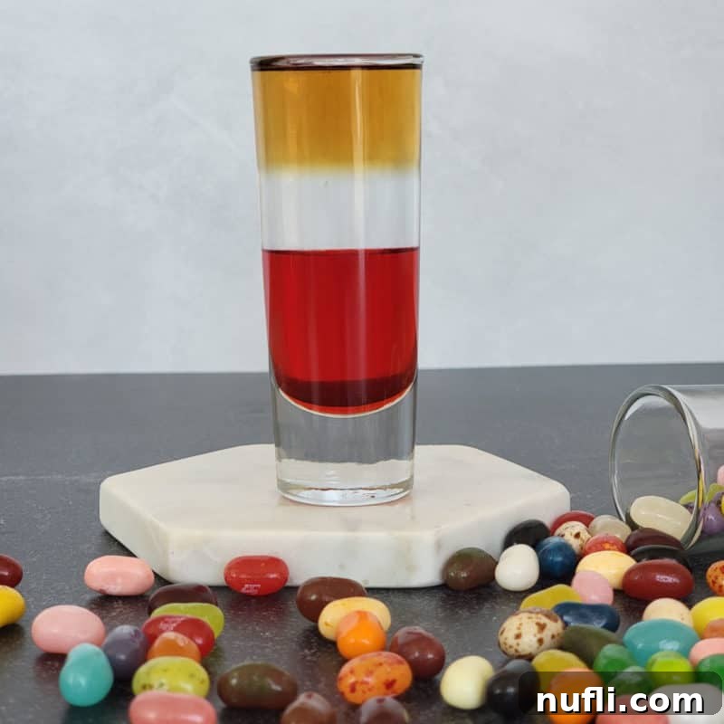 Layered jelly bean shot on a white coaster surrounded by jelly beans