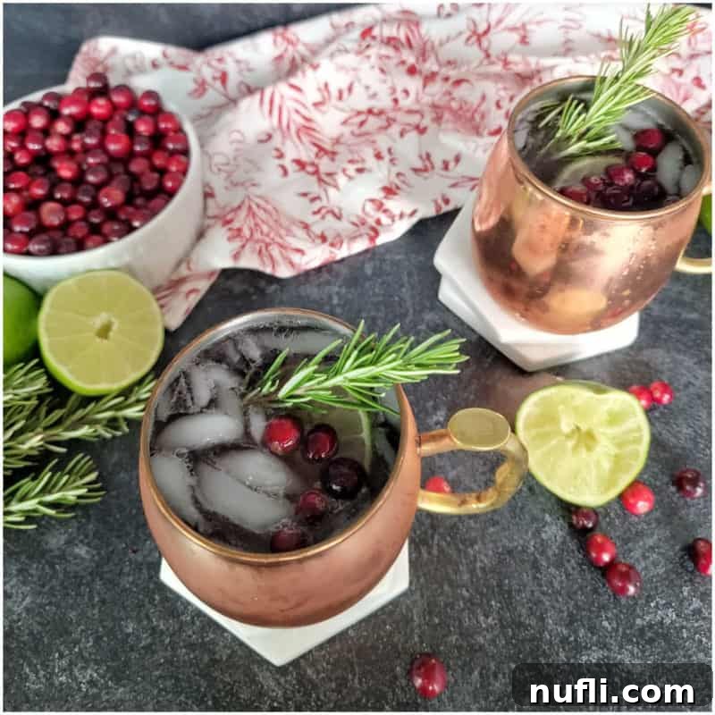 Cranberry Moscow Mules in copper mugs with a bowl of fresh cranberries and lime slices, a festive holiday drink
