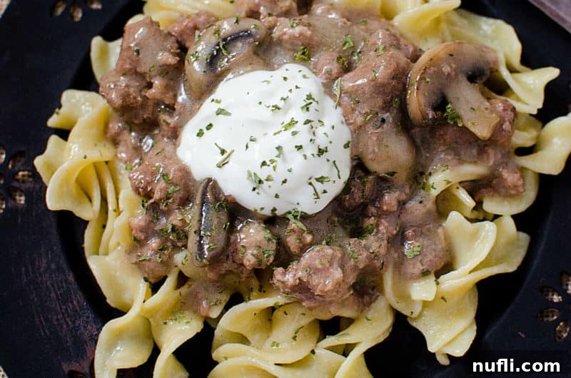 Crock Pot Beef Stroganoff on a blue plate with a dollop of sour cream on top