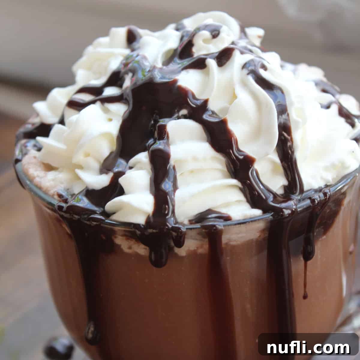 Crockpot hot chocolate in a glass mug topped with whipped cream and chocolate syrup