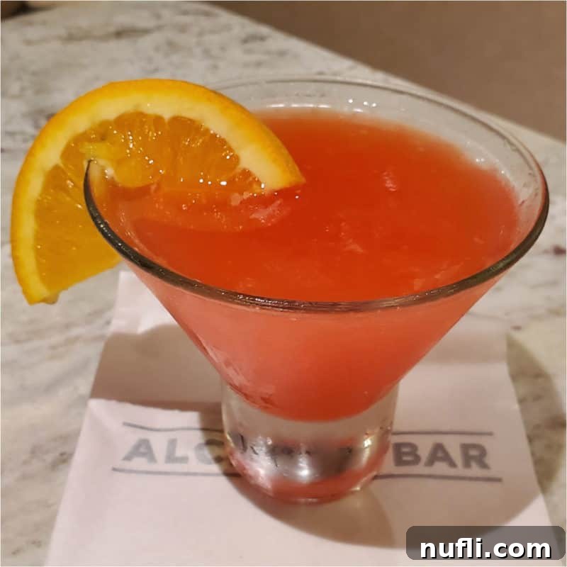 A seductive Martini Seduction Cocktail, featuring an orange wheel garnish in a chic stemless martini glass, resting on a white surface.