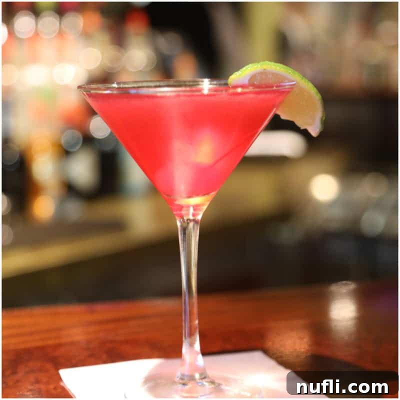 A bright red Pomegranate Breeze Martini, elegantly garnished with a lime wedge, in a classic martini glass atop a crisp white napkin.