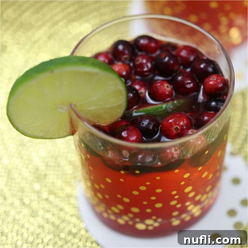 A festive Cranberry Lime Cocktail with fresh cranberries and lime slices in a golden polka-dotted glass, exuding holiday cheer.