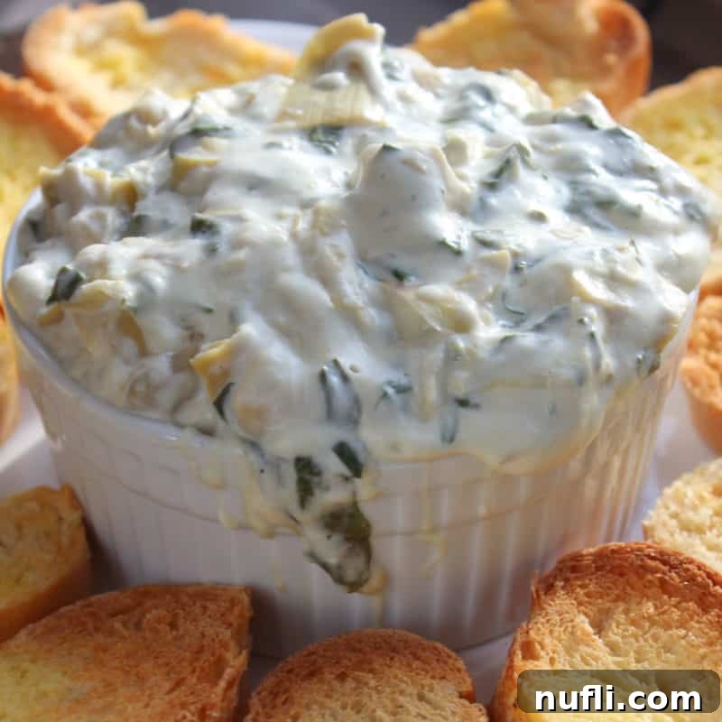Creamy Crock Pot Spinach Artichoke Dip served in a white bowl, accompanied by golden toasted bread slices