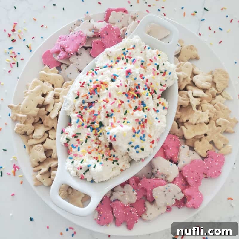 Whimsical Dunkaroo Dip in a white bowl, adorned with rainbow sprinkles and surrounded by an assortment of animal crackers and cookies