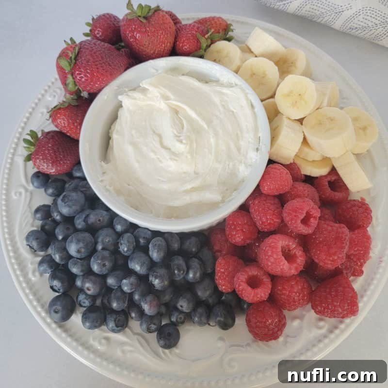 Fluffy Marshmallow Fluff Fruit Dip in a white bowl, beautifully surrounded by a colorful array of fresh blueberries, raspberries, banana slices, and strawberries
