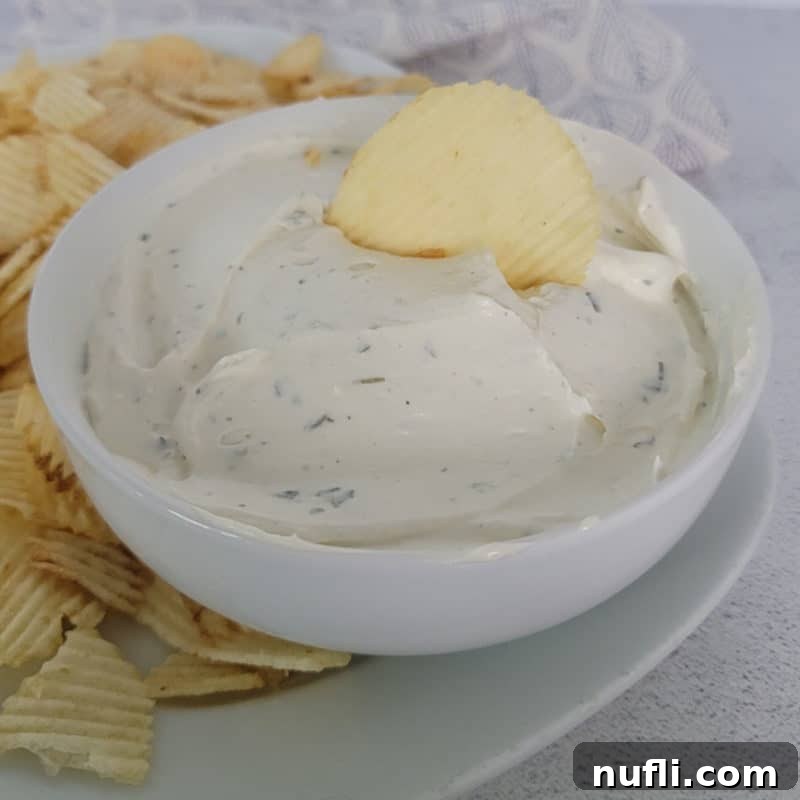 Classic Potato Chip Dip in a white bowl, with a potato chip perfectly scooping into the creamy dip, surrounded by more chips