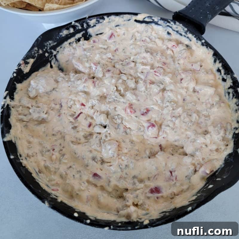 Sizzling Rotel Sausage Dip served hot in a rustic cast iron skillet