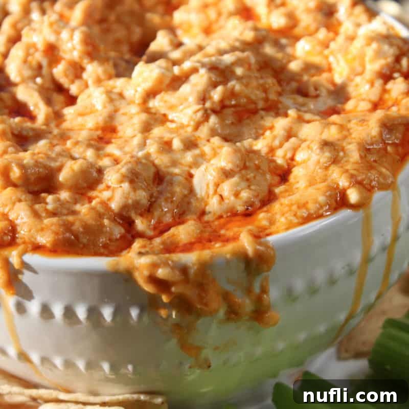 Hearty Crockpot Buffalo Chicken Dip in a white bowl, accompanied by crisp celery sticks for dipping