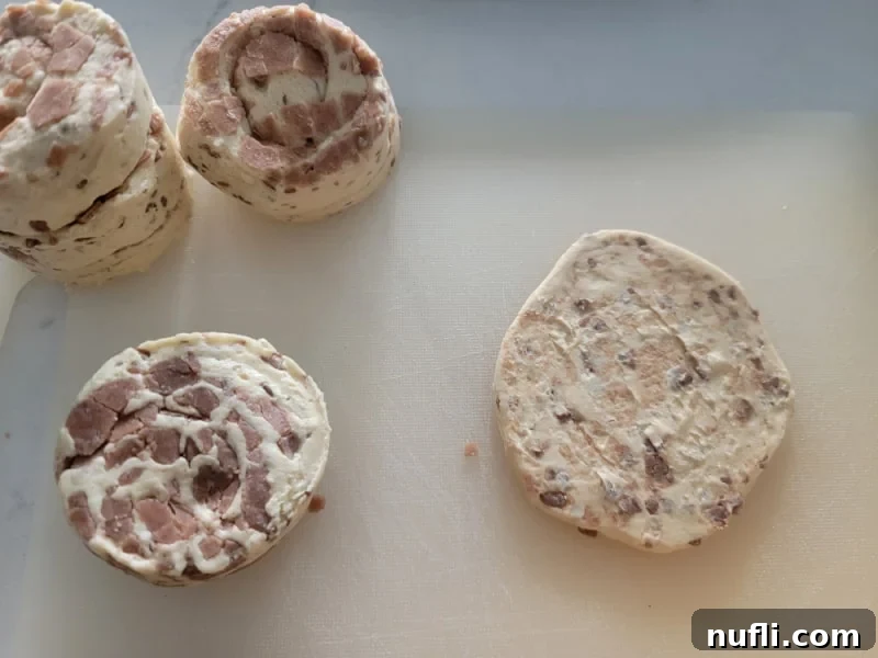 2-Ingredient Cinnamon Roll Apple Pie Bites 4 Refrigerator cinnamon rolls on a cutting board, with one flattened and ready to become a cinnamon roll apple pie cup.