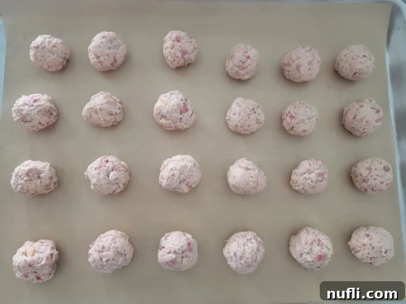 Unbaked Cheddar Bay Sausage Balls neatly arranged on a parchment-lined baking sheet, ready for the oven.