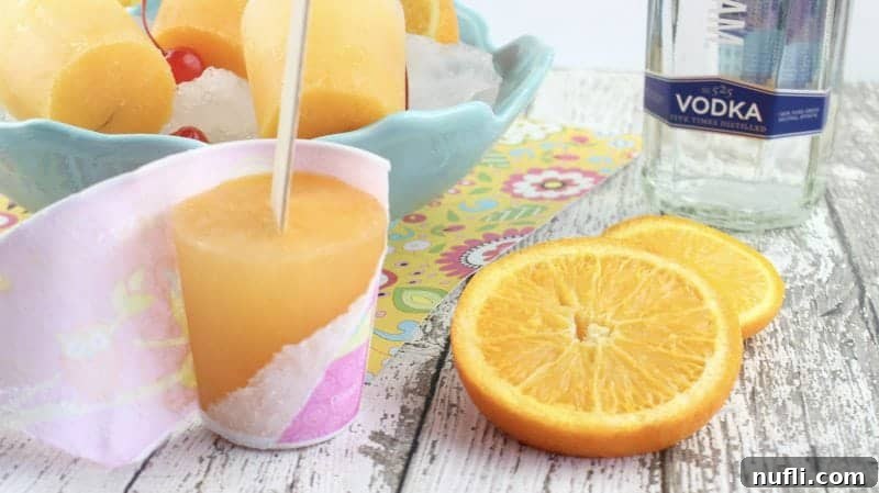 Screwdriver Popsicles next to oranges and a bottle of vodka
