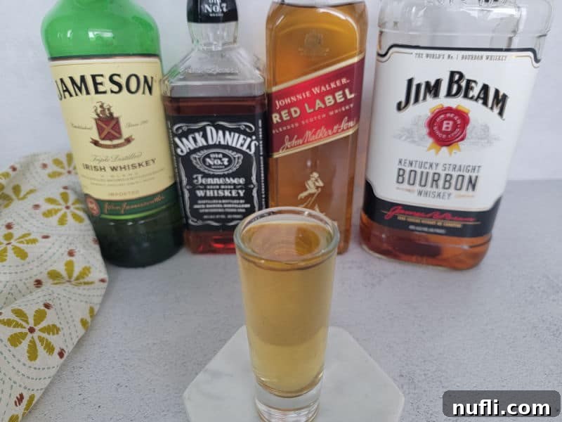 Four horsemen shot in a shot glass on a white coaster in front of bottles of Jameson Irish Whiskey, Jack Daniels, Johnnie Walker and Jim Beam