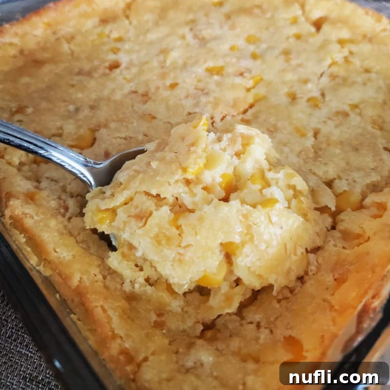 A silver spoon lifting out a generous serving of Creamed Corn Casserole from a baking dish, showcasing its rich texture.