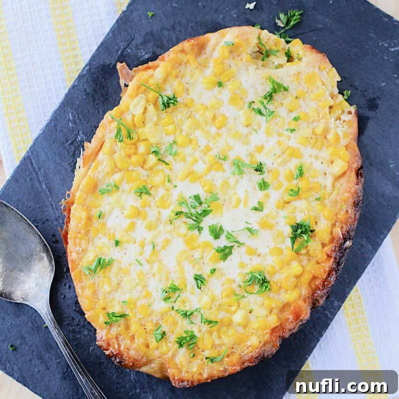 A portion of golden corn pudding elegantly presented on a slate board alongside a serving spoon.