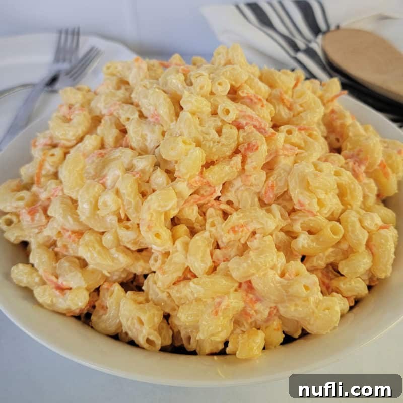 Creamy Hawaiian Mac Salad in a white bowl, artfully placed next to plates and a wooden spoon, ready to be served.