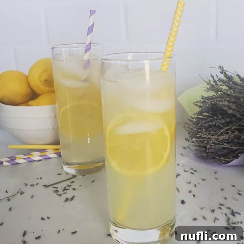 Two elegant Lavender Lemonade Cocktails in tall glasses with colorful paper straws, beautifully arranged next to a bowl of fresh lemons, creating a refreshing and aromatic spring scene.