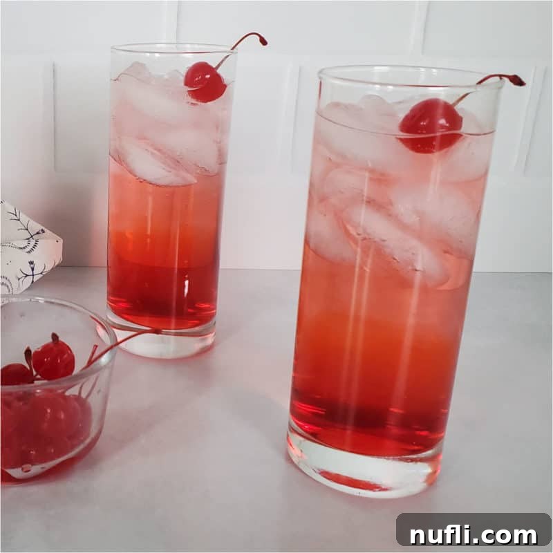 Two vibrant red Dirty Shirley cocktails in tall glasses, expertly garnished with bright maraschino cherries, displayed beside a bowl overflowing with these classic red cherries.