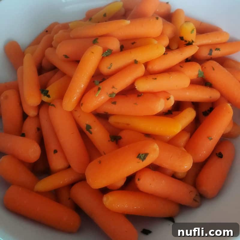 Vibrant cooked carrots garnished with fresh greens in a white serving bowl