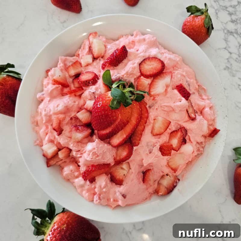 Strawberry Cloud Delight 2 Strawberry fluff salad in a white bowl with cut strawberries for garnish
