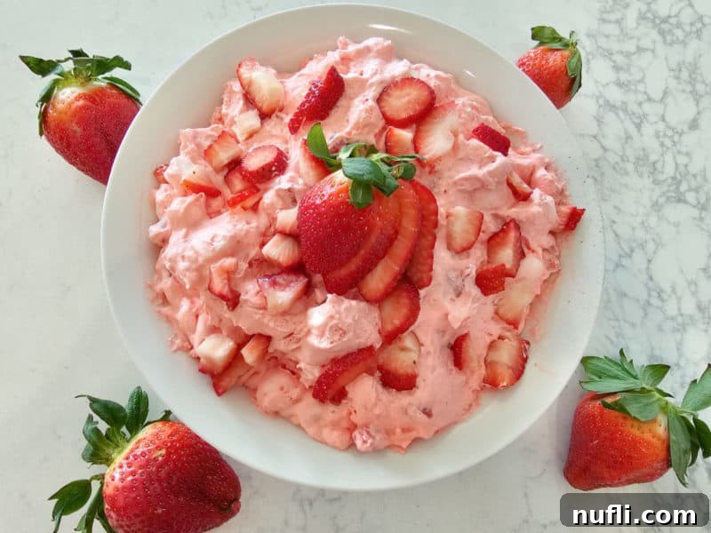 Strawberry Cloud Delight 8 Strawberry fluff salad in a white bowl topped with fresh strawberries on a white counter