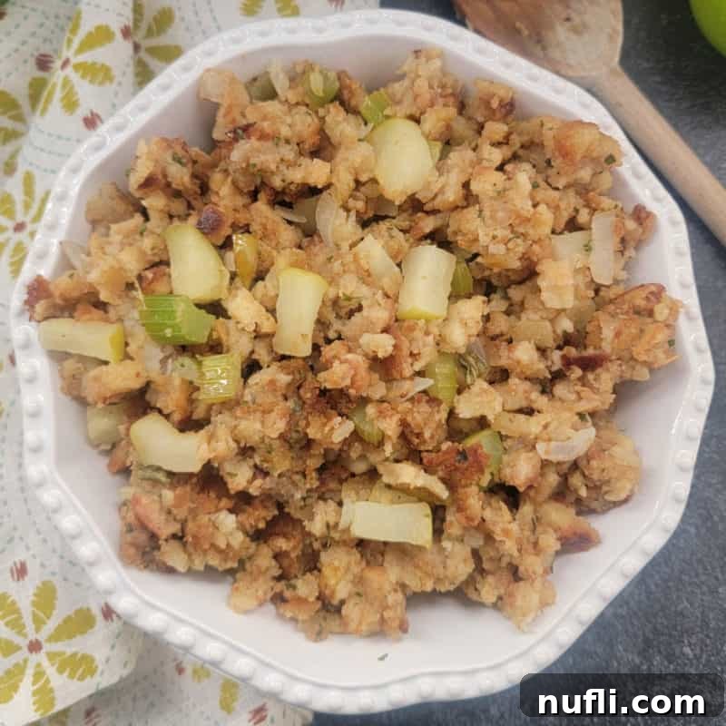 Savory Apple Stuffing in a white bowl, elegantly presented alongside a cloth napkin and a wooden spoon.
