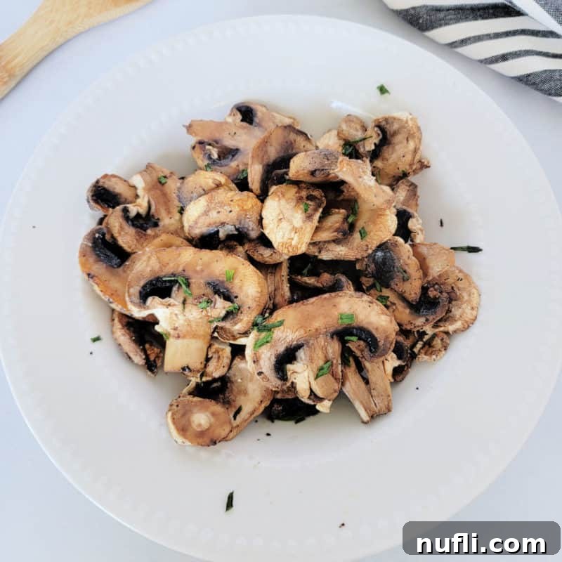 air fried mushrooms in a white bowl next to a wooden spoon and napkin